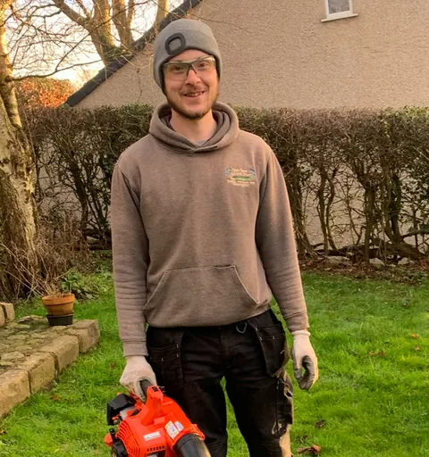 Jamie standing on a lawn holding a leaf blower